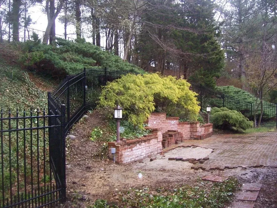 Black fence frames a brick structure with lights, lush greenery on a hillside.