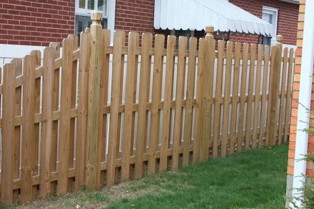 Wooden picket fence in a grassy yard, beside a brick building.