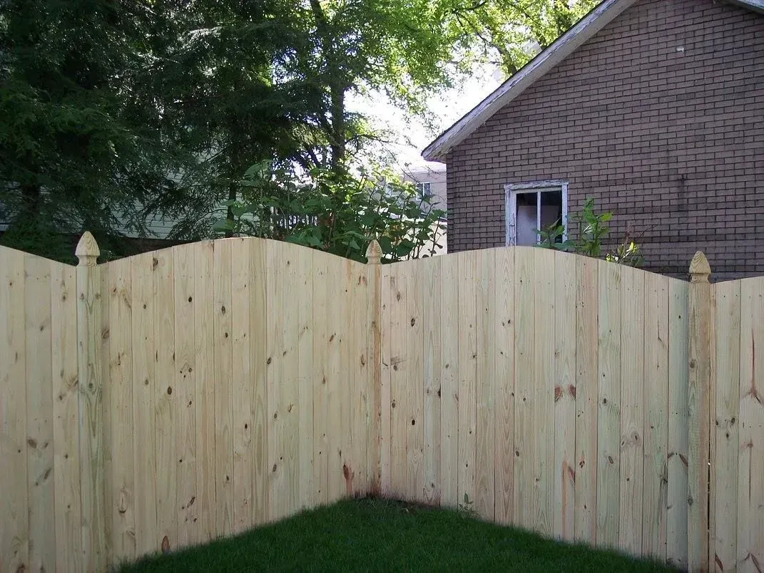 Wooden fence in a yard with a house in the background. Green grass and trees are also visible.