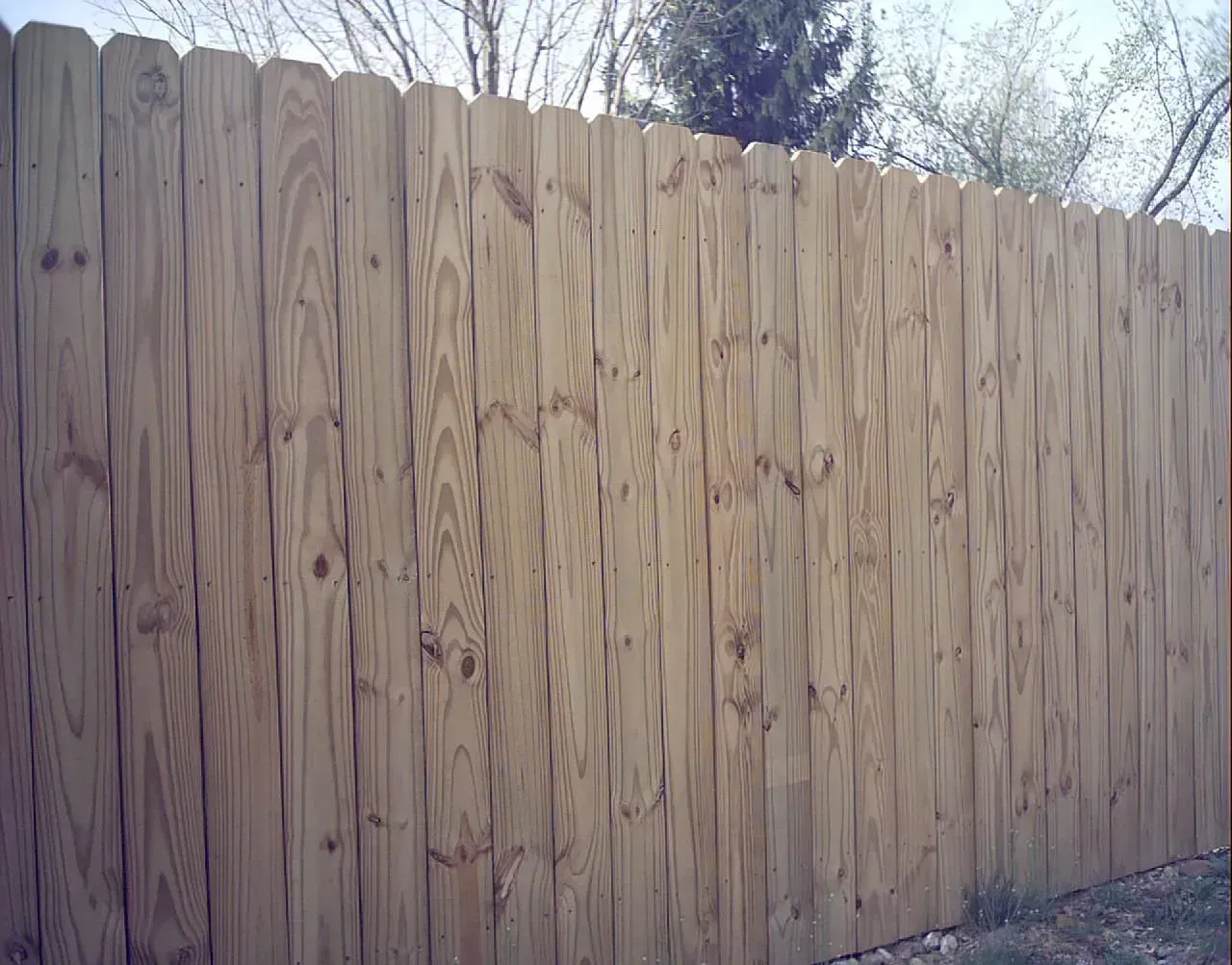 Wooden fence with pointed top, outdoors, natural wood color.