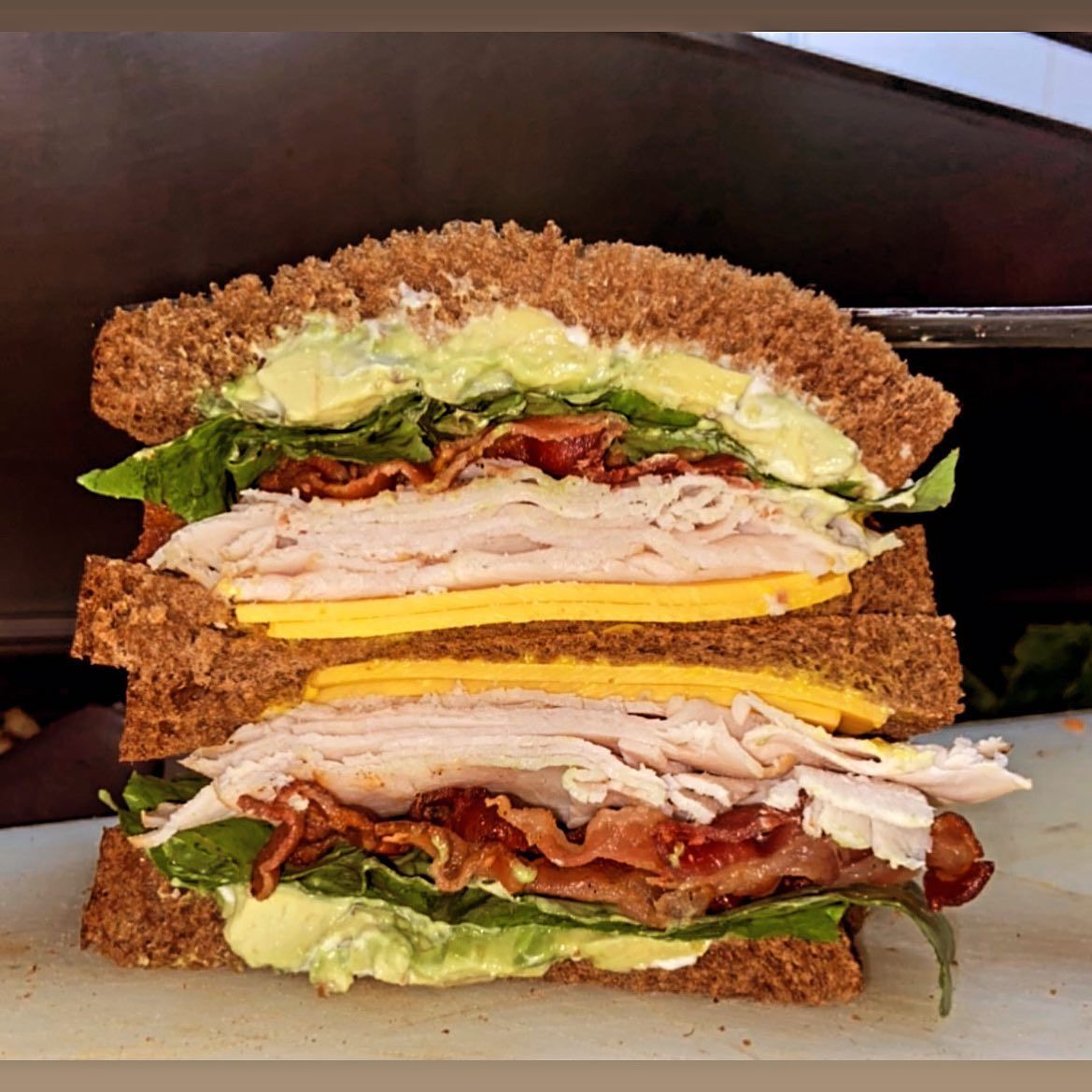 A sandwich with turkey bacon cheese and lettuce on a cutting board