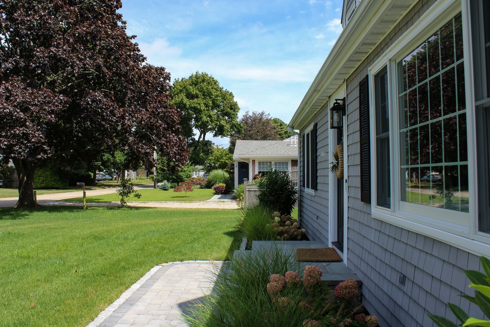 Gray shingled house exterior with white window frames and a walkway, sunny day.