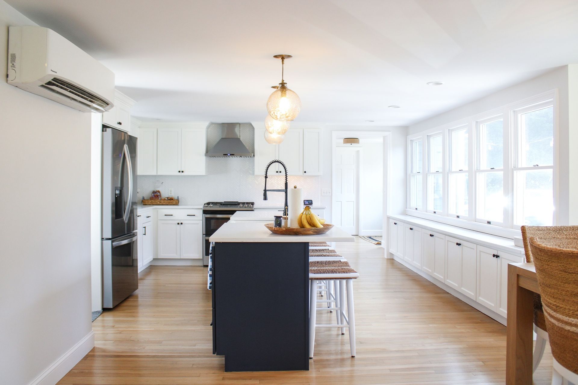 Bright kitchen with white cabinets, dark blue island, stainless steel appliances, and wood floor.