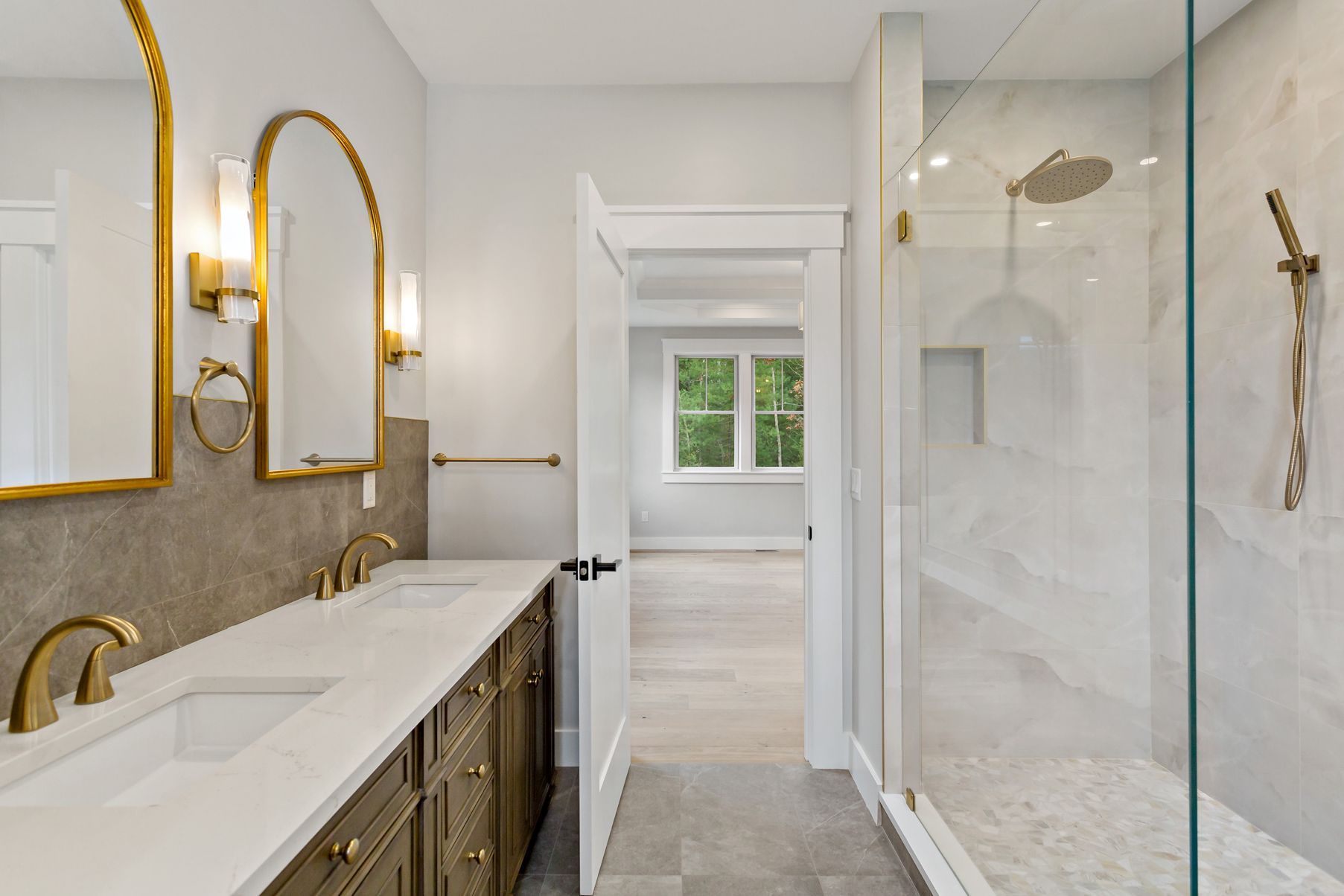 Bathroom with gold fixtures, marble shower, and long vanity with arched mirrors.