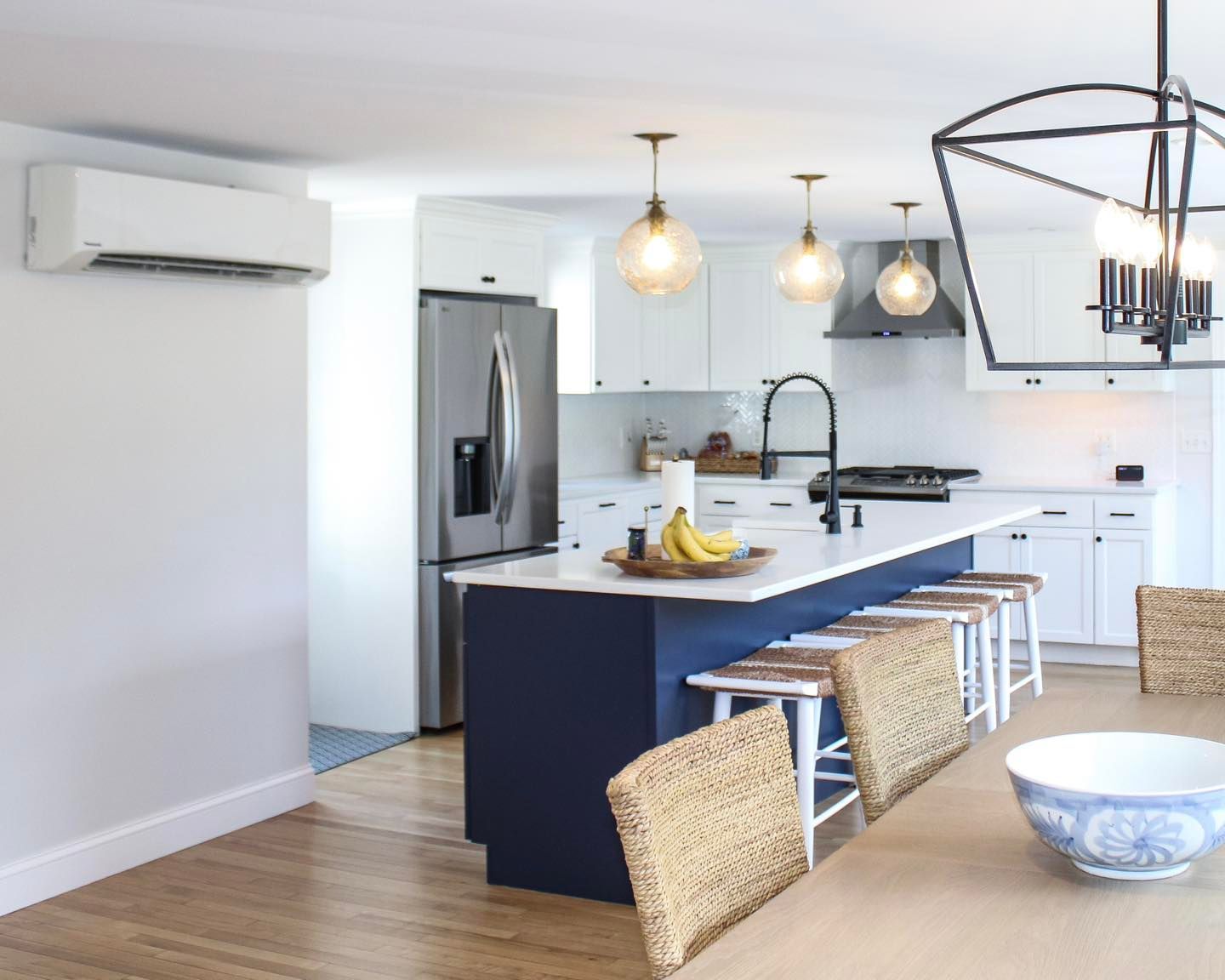 Modern kitchen with white cabinets, blue island, stainless steel appliances, and gold pendant lights.