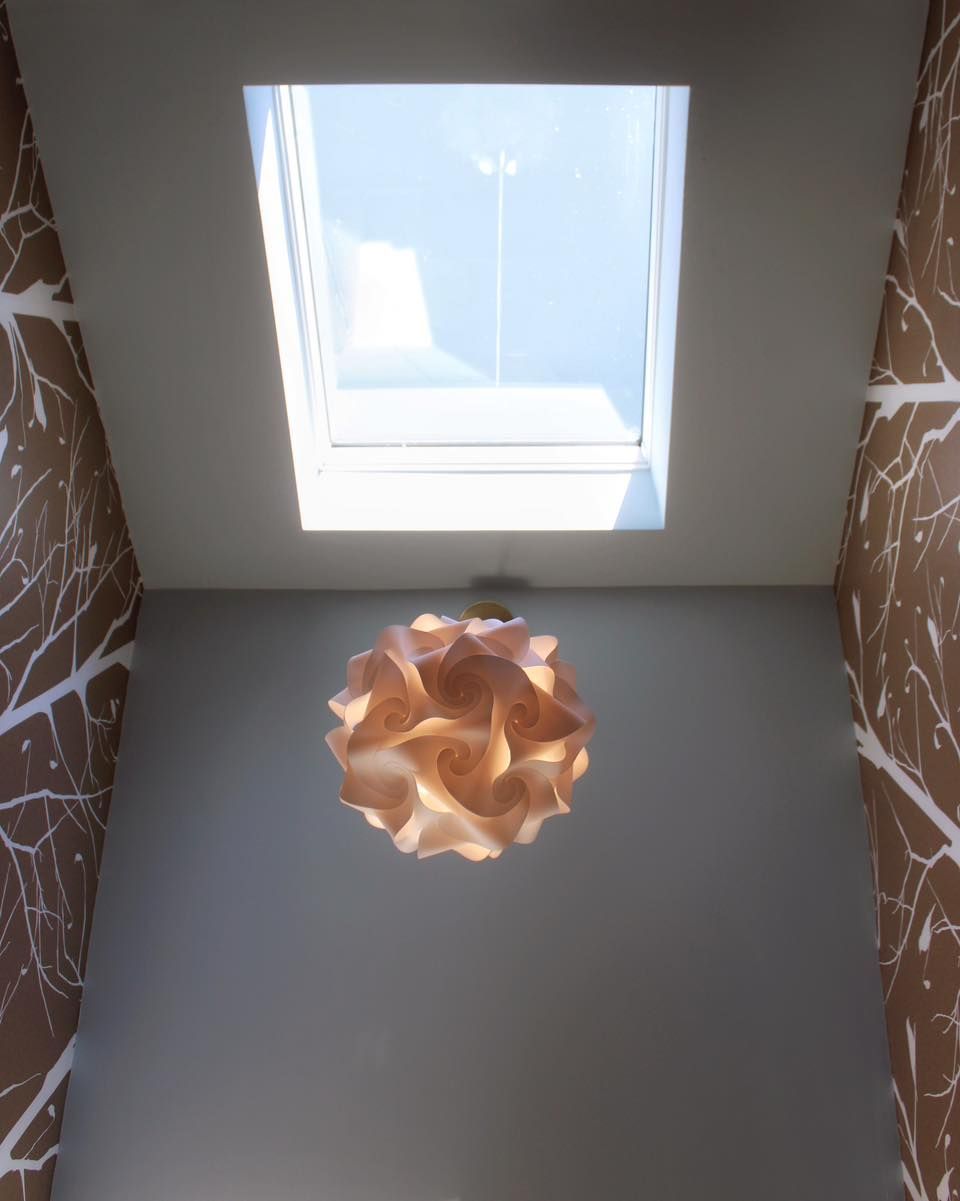 Skylight in a white ceiling above a textured brown wall, a geometric lamp hangs below.