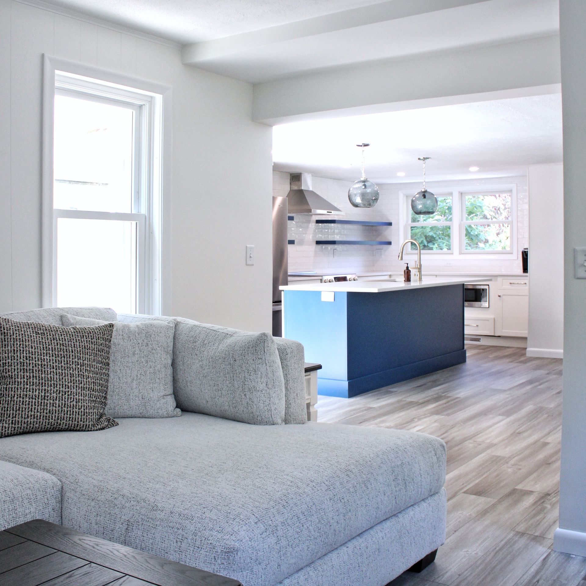 Living room with light gray sectional sofa, open to blue kitchen.
