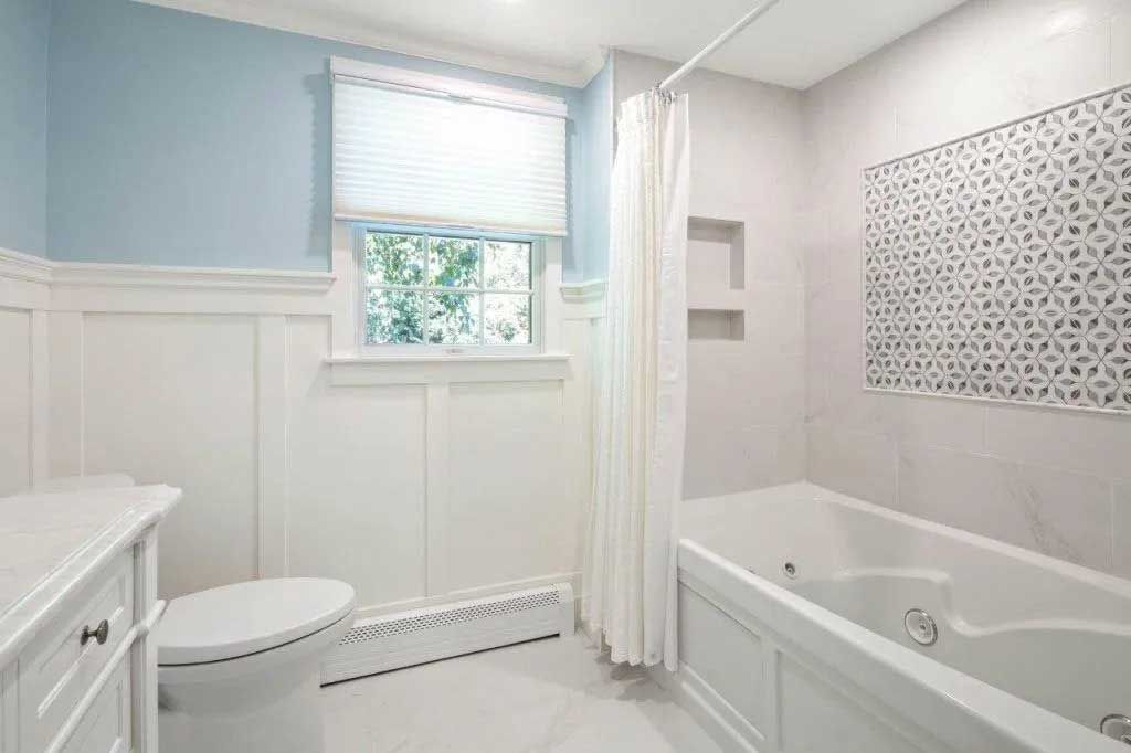 Bathroom with white and blue walls, tub, toilet, and patterned tile accent.