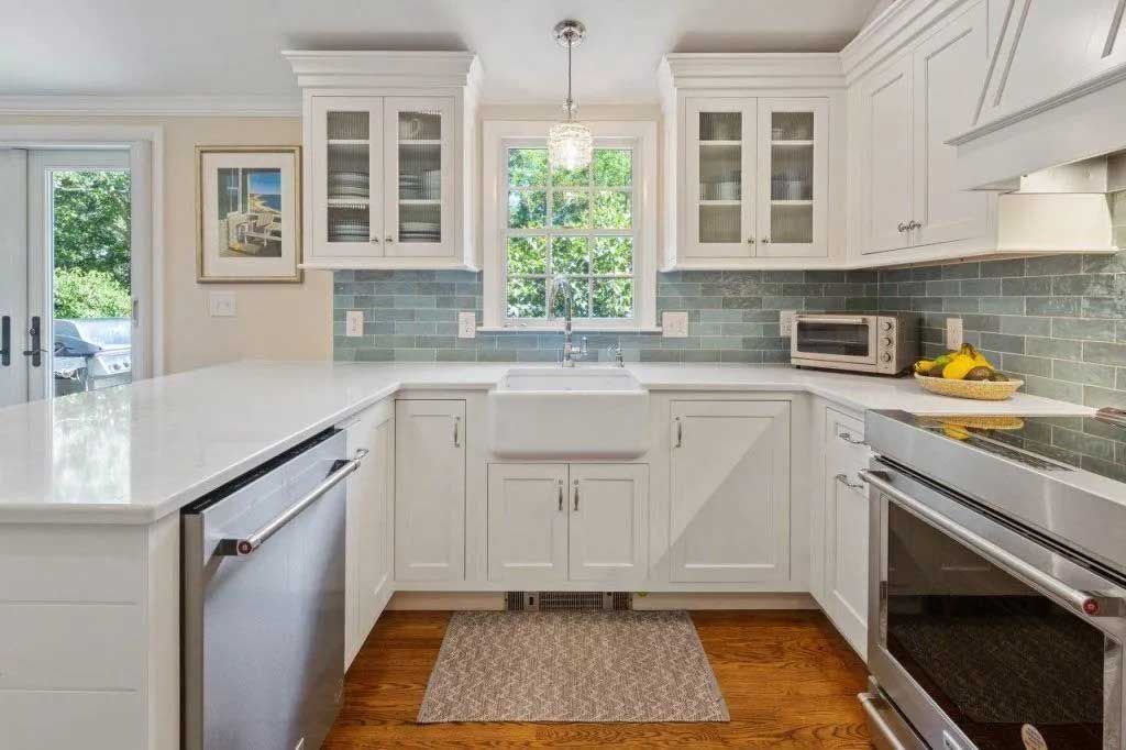 White kitchen with a U-shaped layout, featuring a farmhouse sink, stainless steel appliances, and blue tiled backsplash.