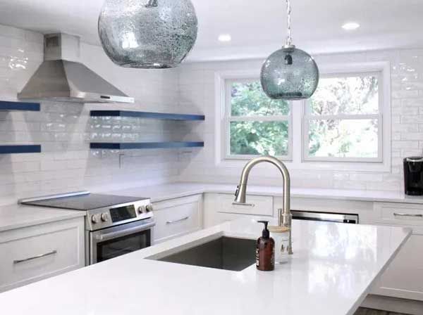 Modern kitchen with white counters, blue shelves, and two blue glass pendant lights.