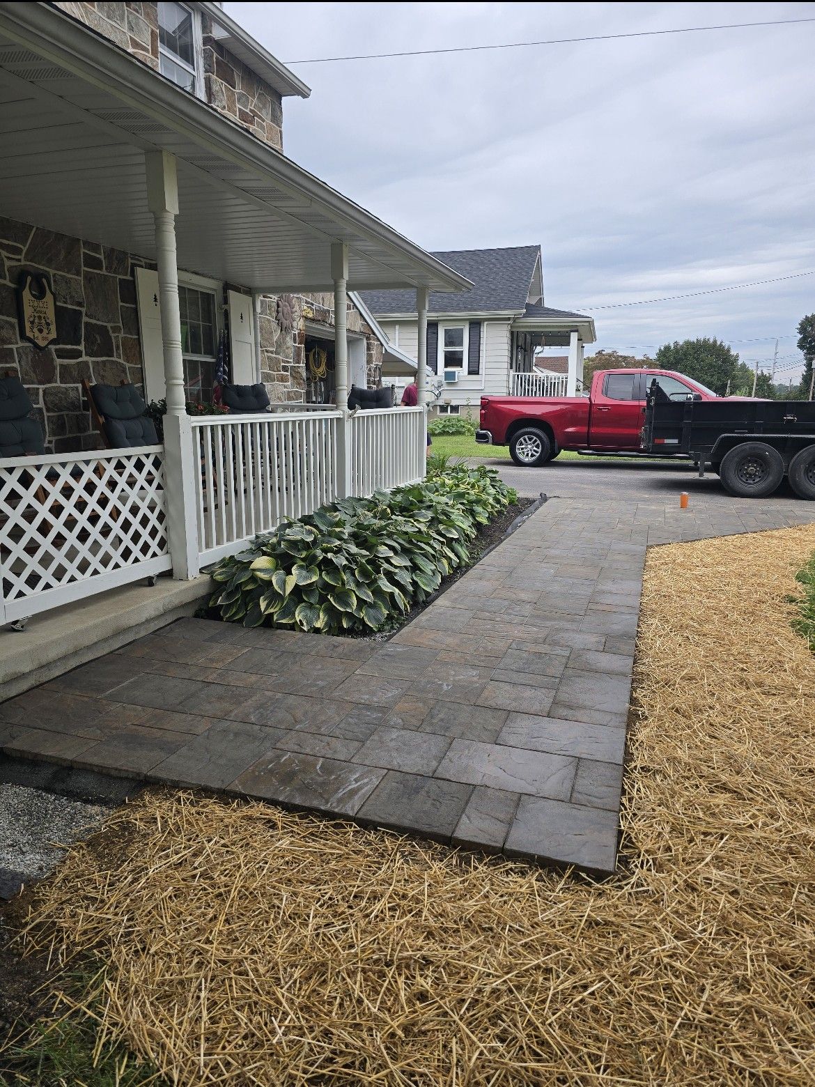 Front porch and stone walkway beside a house, with red pickup trucks parked in a gravel driveway.