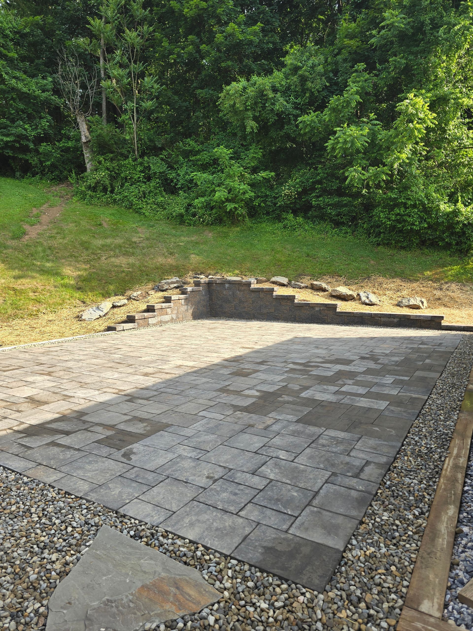 Stone patio with steps beside a grassy slope and dense green trees