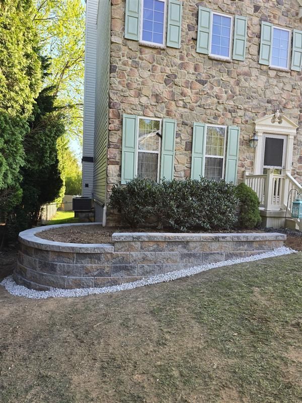 A stone house with green shutters and a brick wall in front of it.