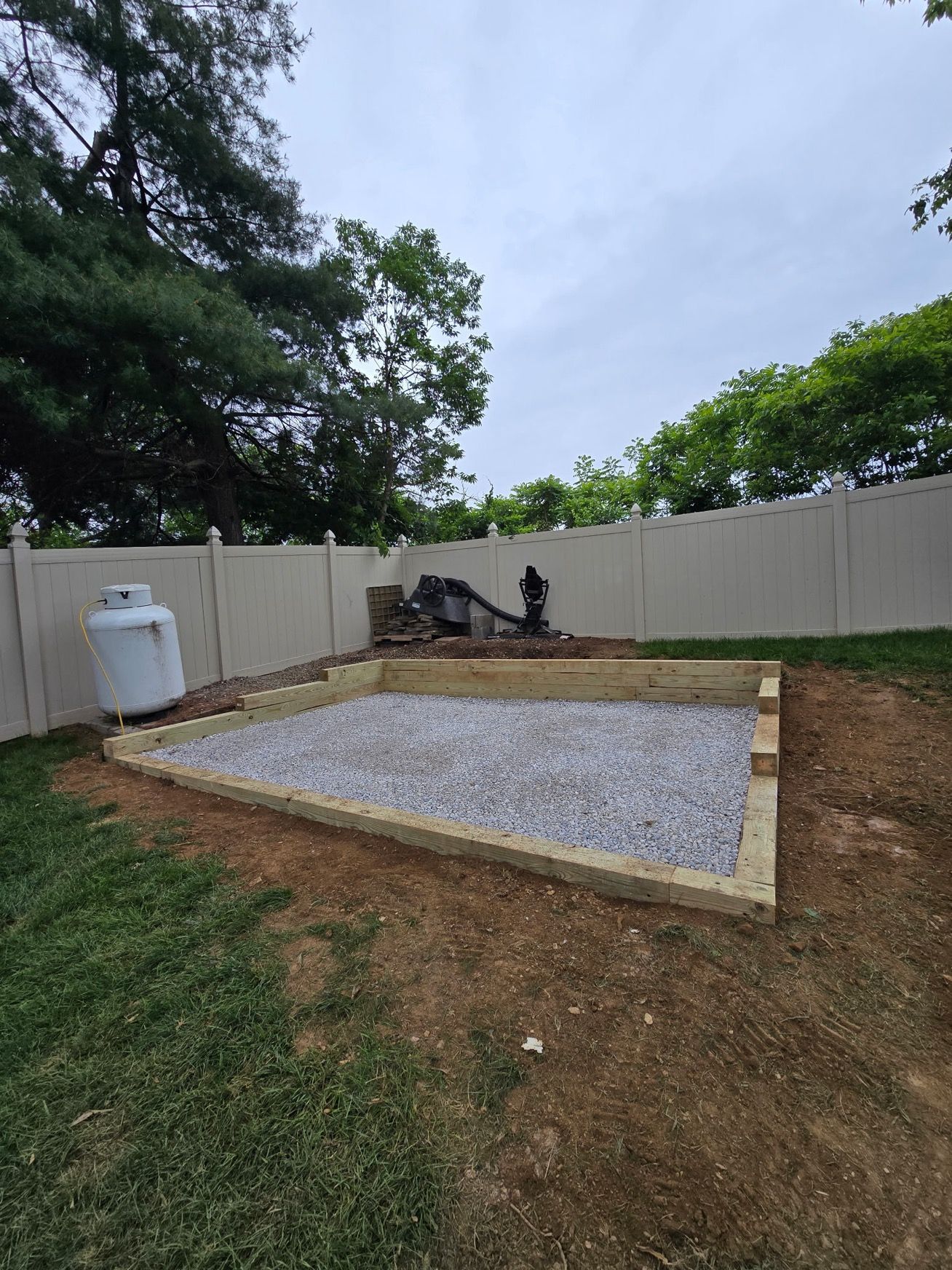 A backyard with a fence and a gravel area in the middle of it.