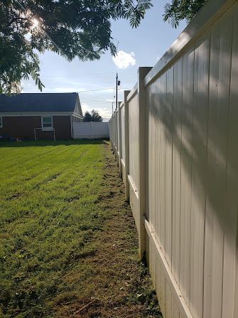 A white fence surrounds a lush green field in front of a house.