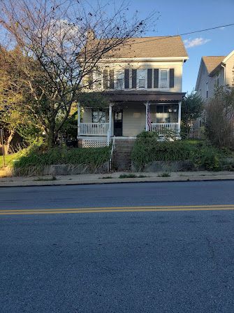 A large white house with a porch is on the side of the road.