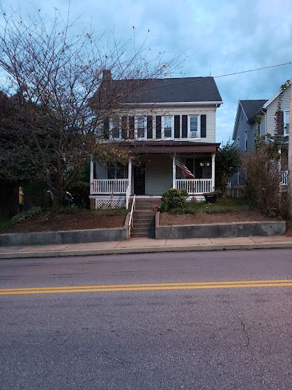 A house with a porch and stairs is on the side of the road.