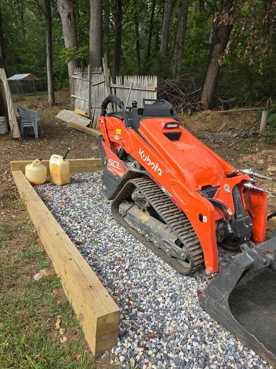 A small orange tractor is parked on gravel in a yard.