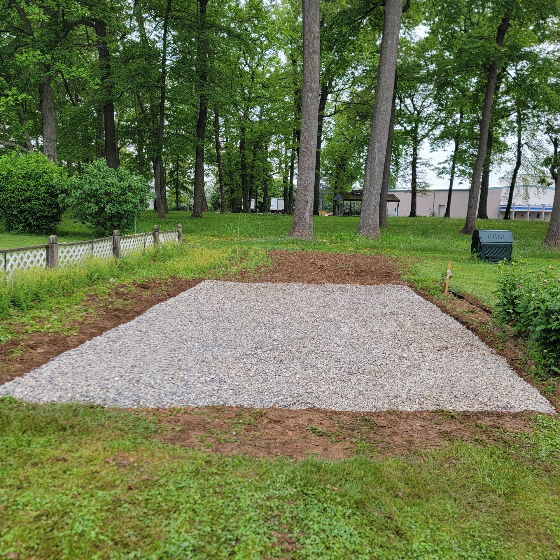 A gravel area in the middle of a lush green field with trees in the background.