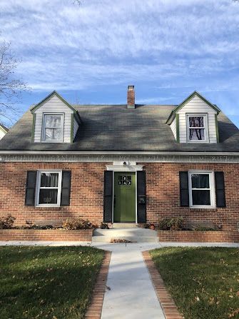 A brick house with a green door and black shutters.