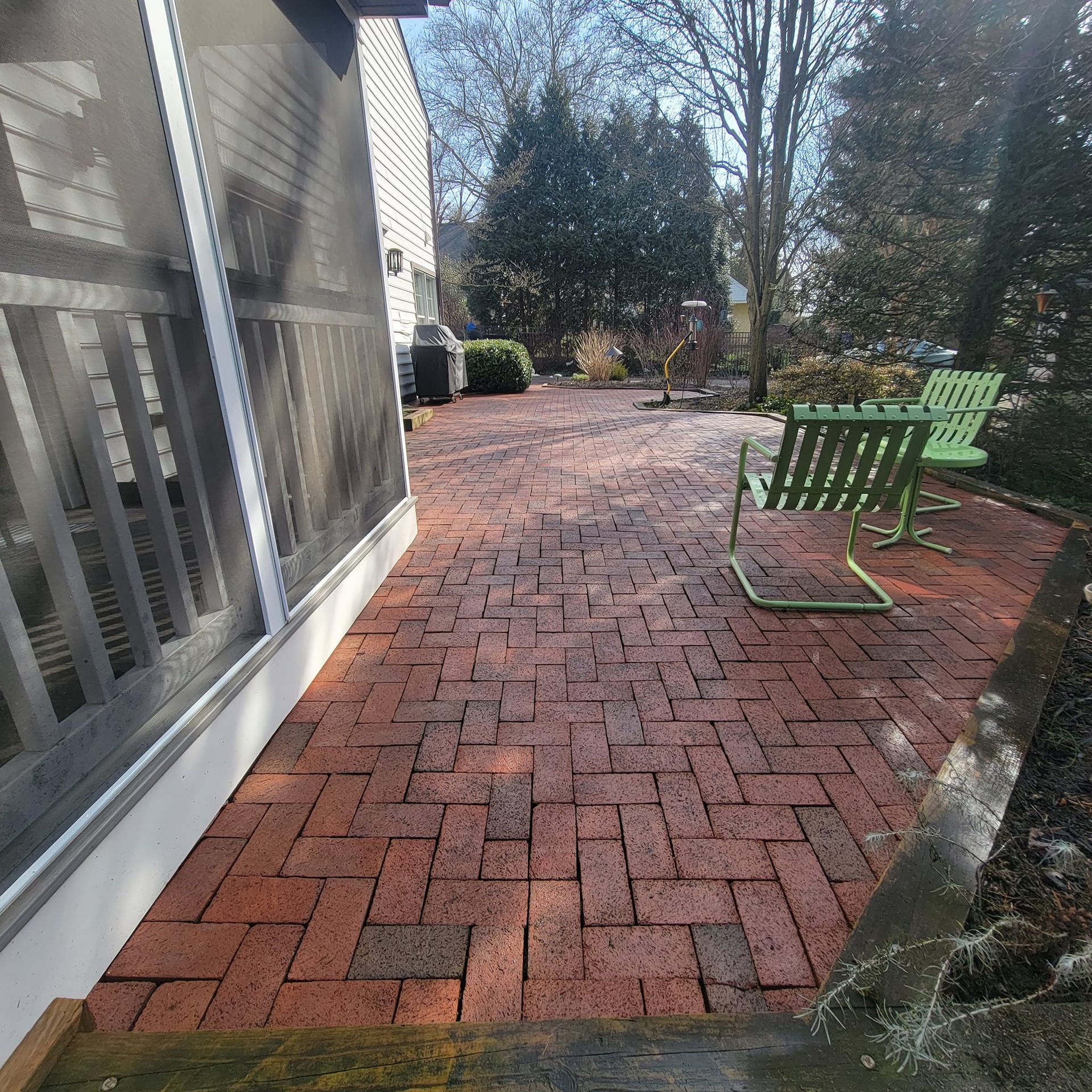 A brick patio with a green chair and a screened in porch