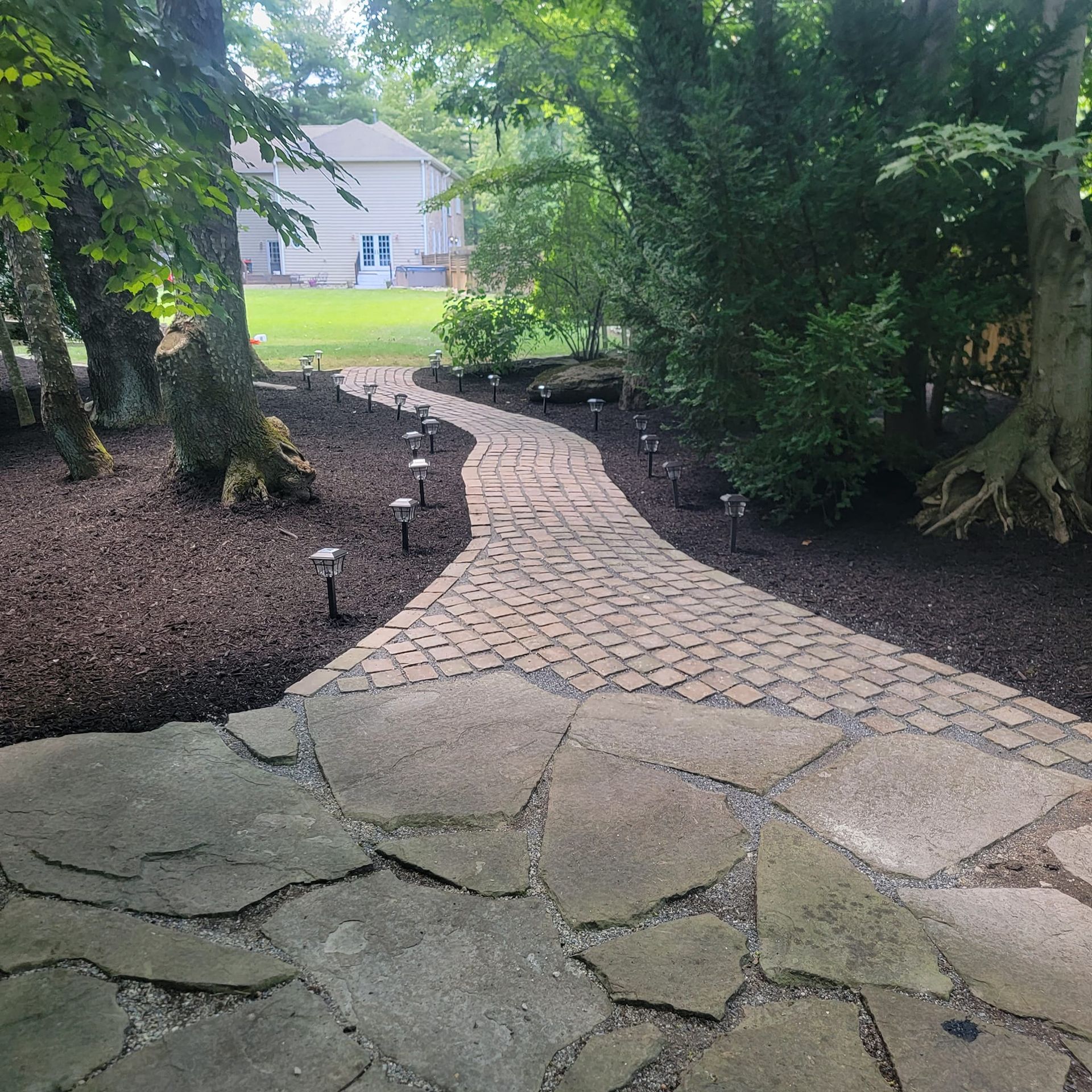A stone walkway leading to a house in the woods.