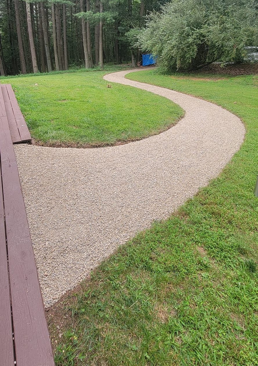 A gravel path going through a lush green field.