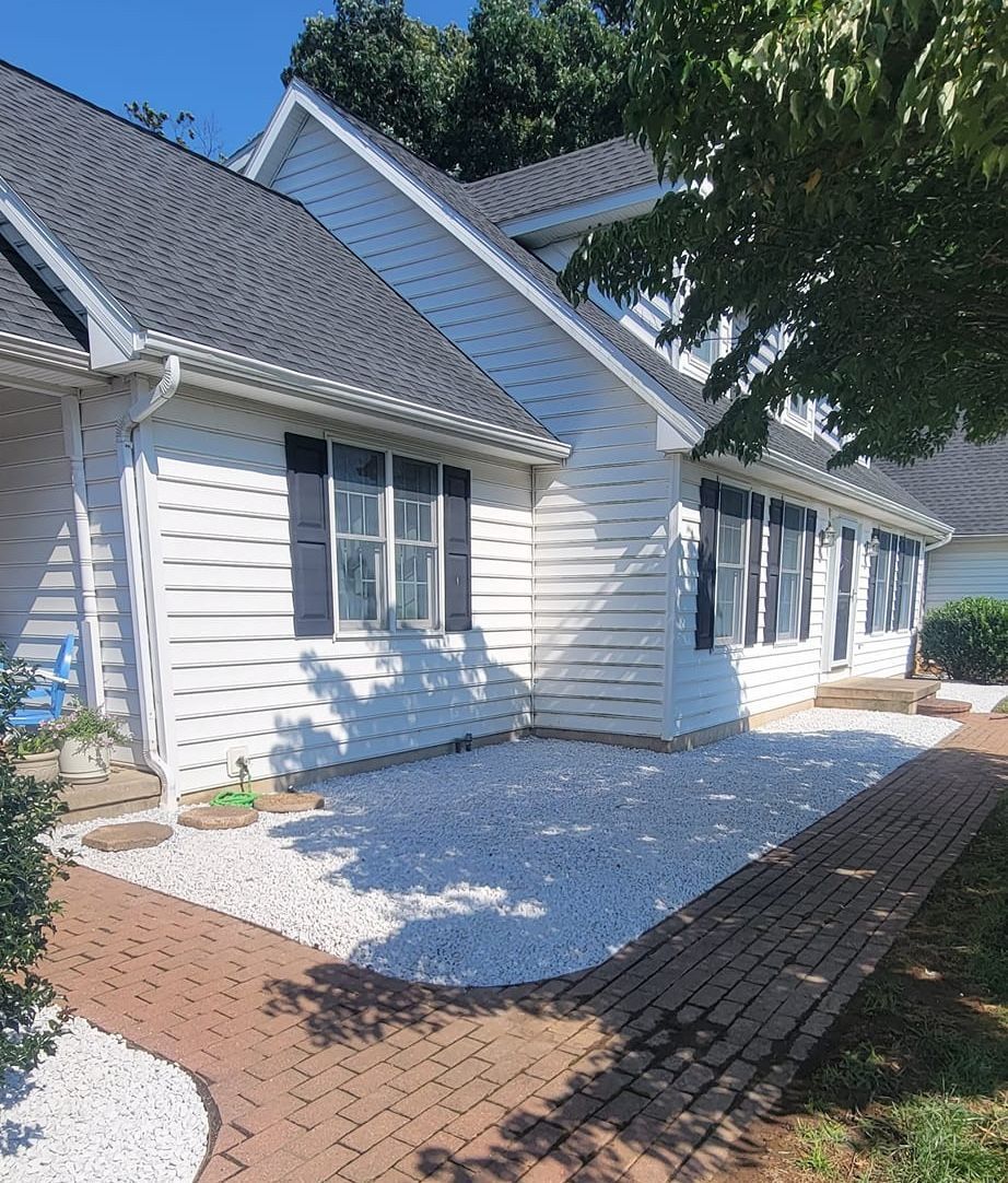 A white house with black shutters and a brick walkway leading to it.