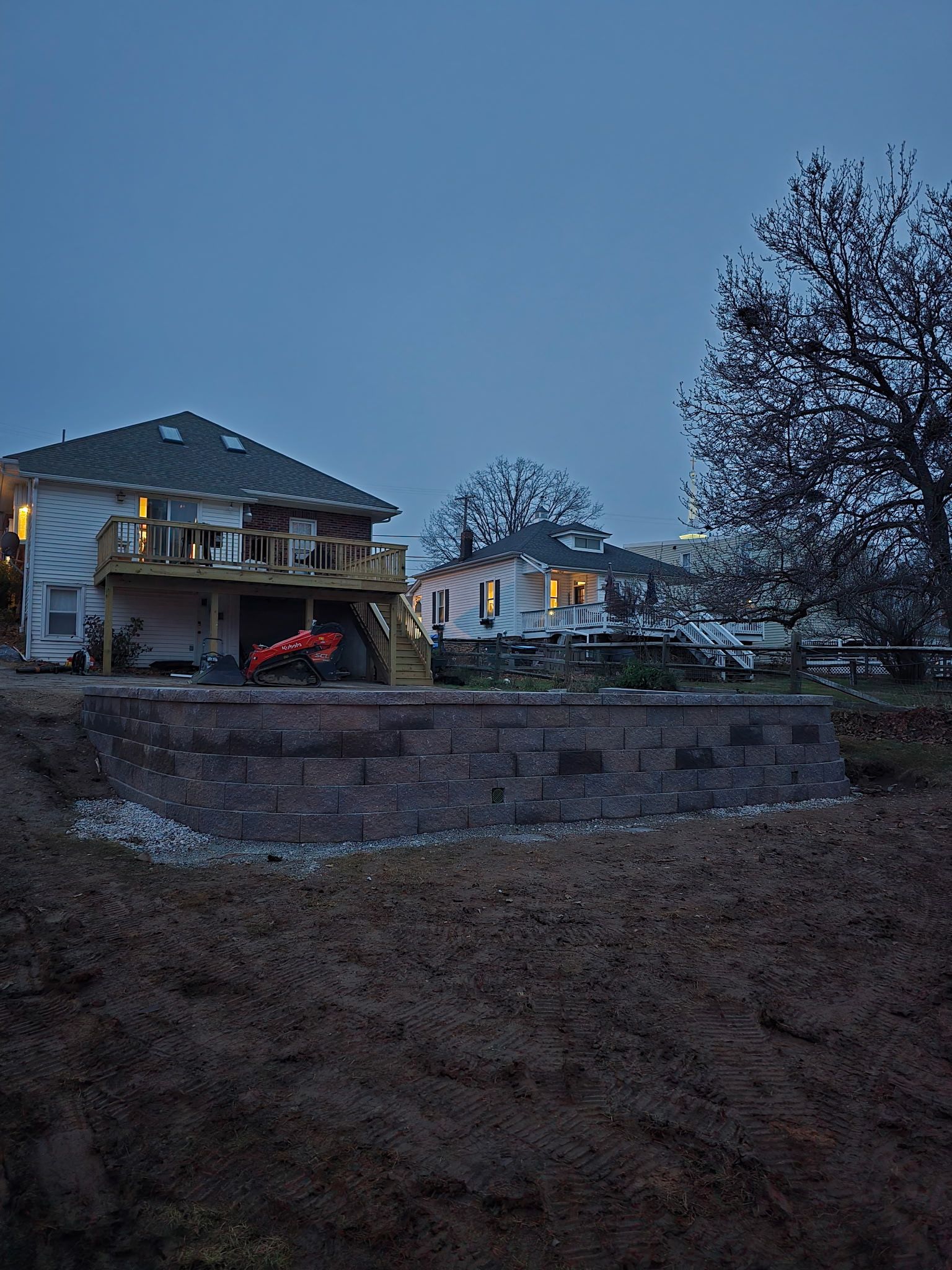 Houses on a slope with retaining wall; twilight sky.