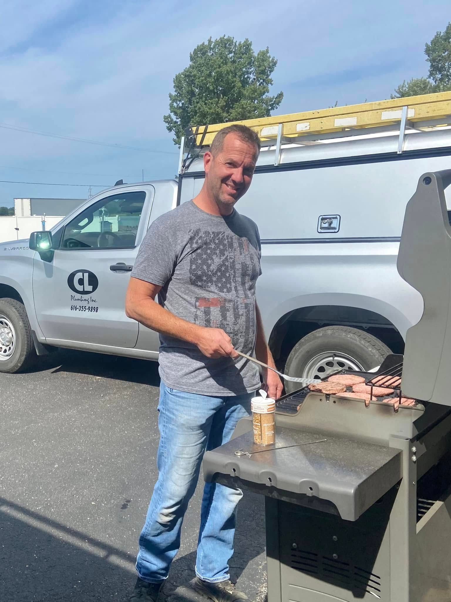 Man grilling food beside a work truck in a parking lot on a sunny day