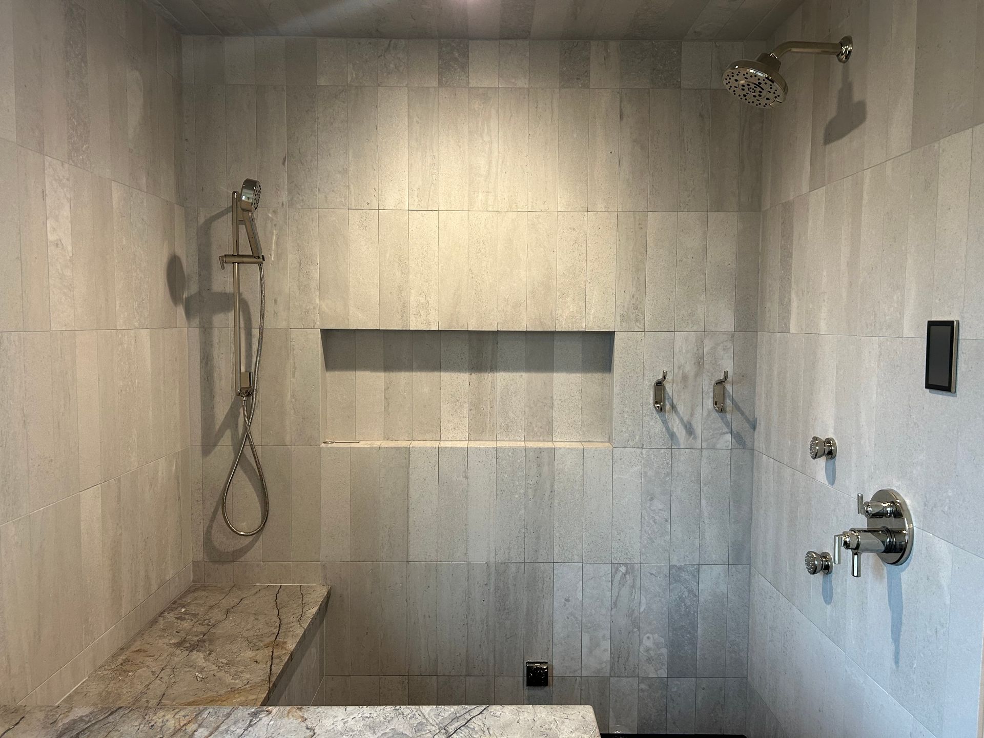 Modern tiled walk-in shower with built-in shelf, bench, and chrome fixtures