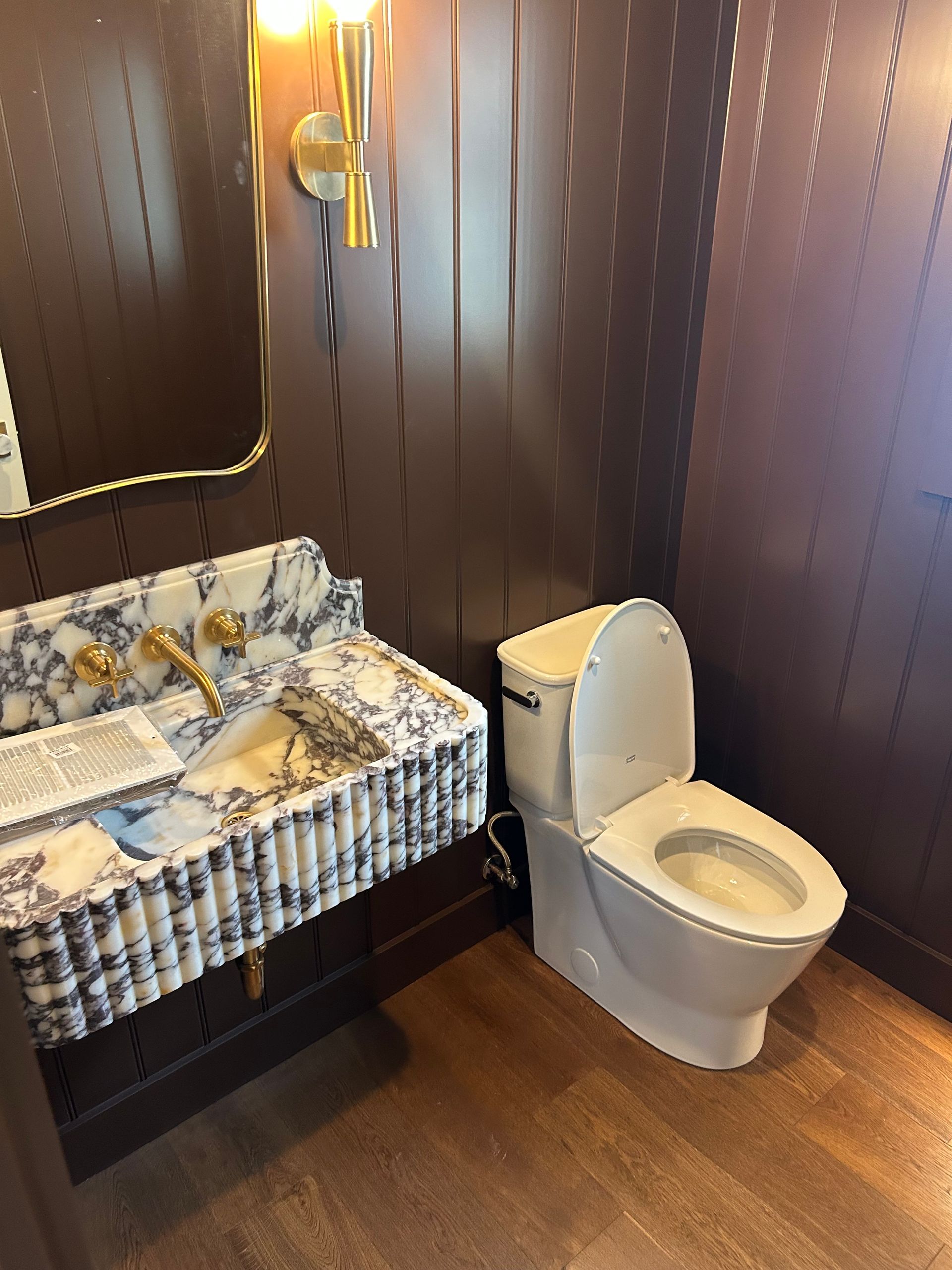 Small bathroom with patterned sink vanity, toilet, and dark wood-paneled walls.