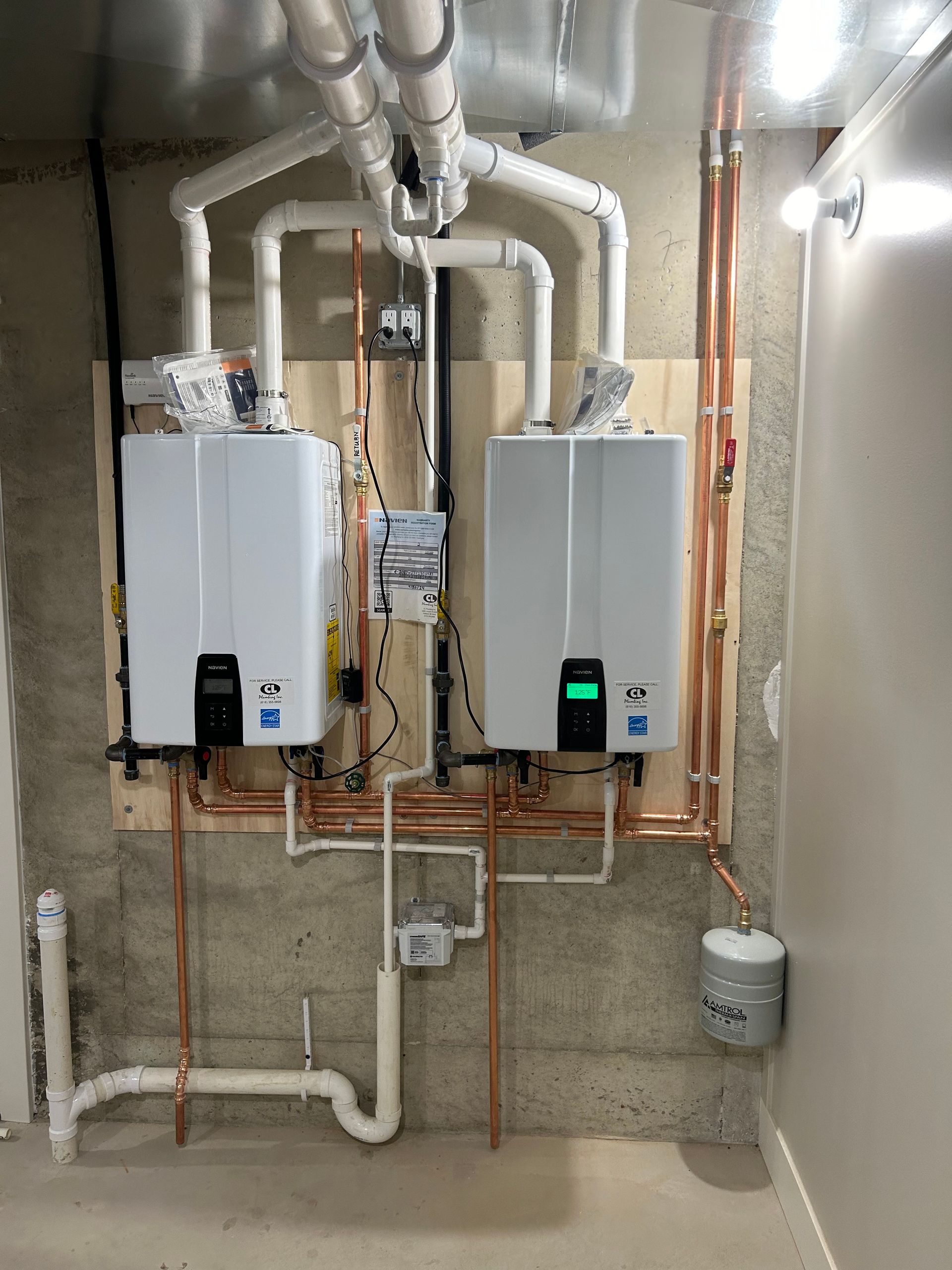 Two wall-mounted tankless water heaters with copper piping in a utility room