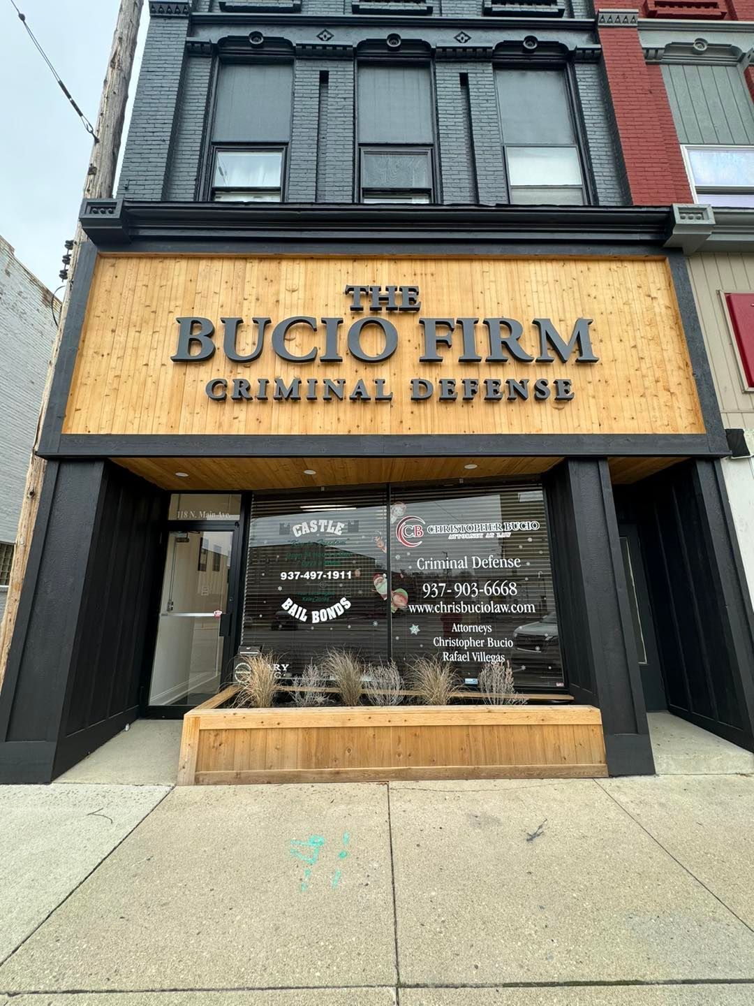 The storefront of The Bucio Firm, a criminal defense law office, with a wooden sign on a black building facade.
