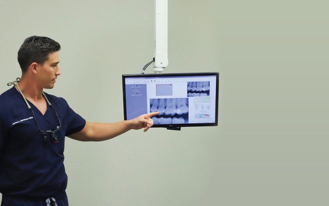 Dentist points at dental x-rays on a monitor in an office.