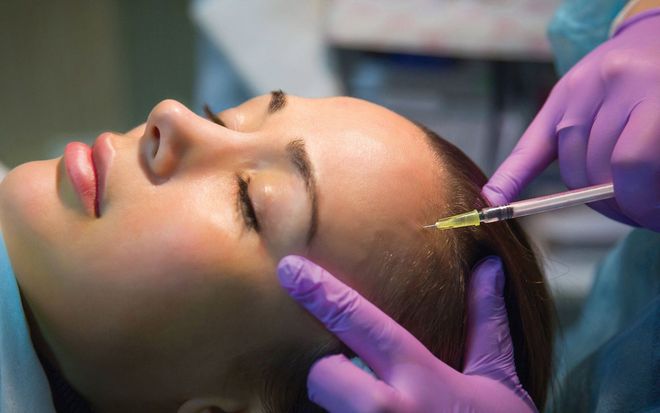 Woman receiving injection in the forehead, performed by gloved hands.