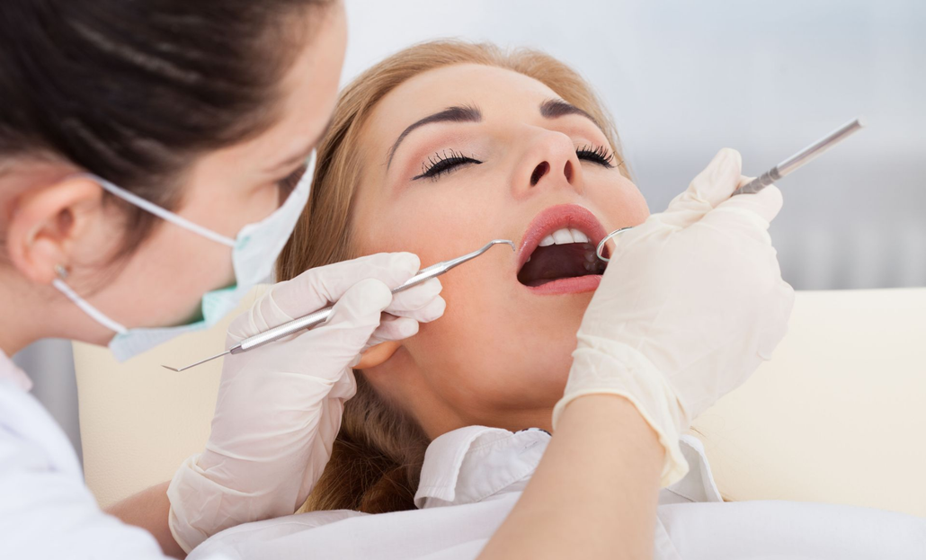Dentist examining a patient's teeth in an office. The patient has mouth open and eyes closed.