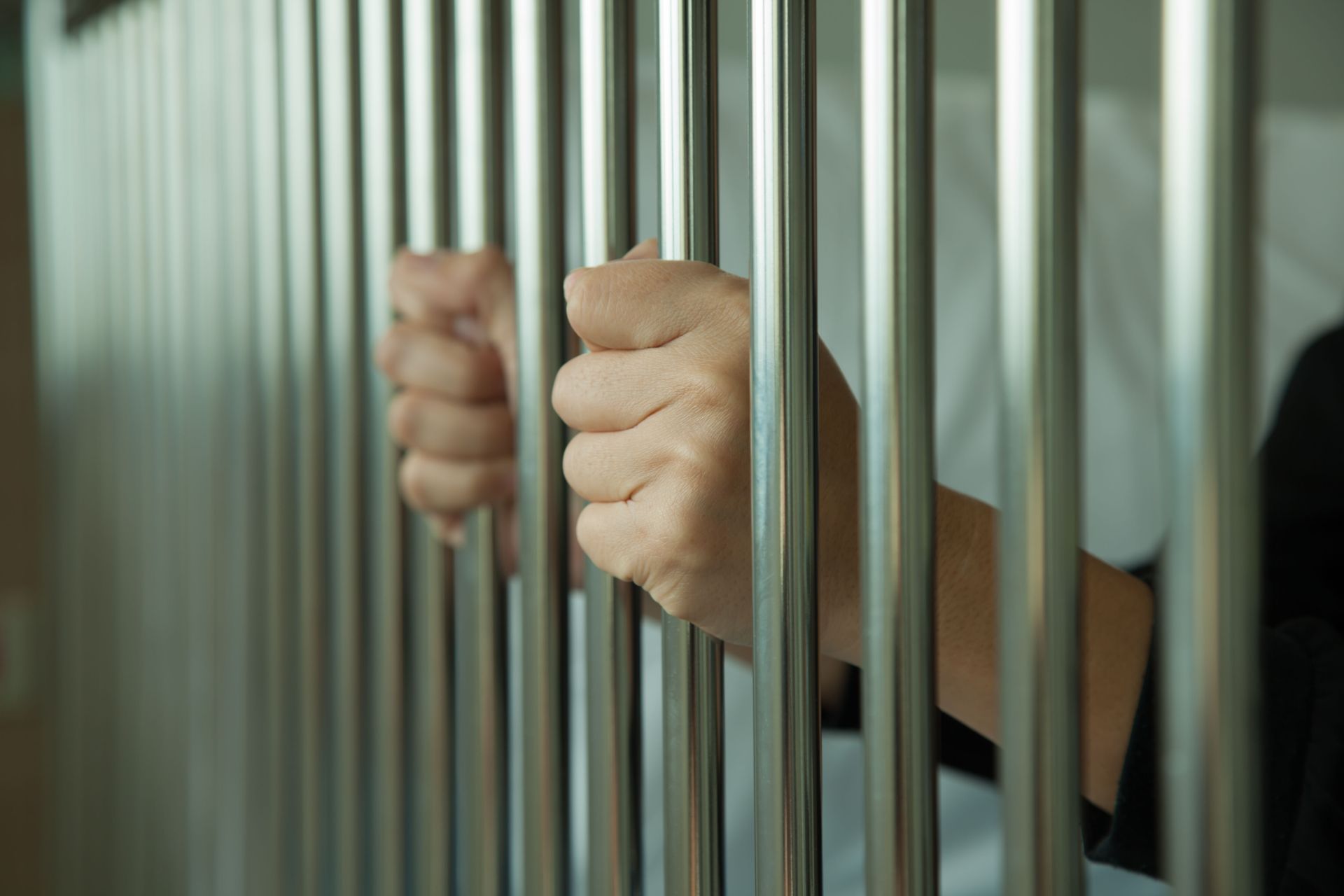 Hands gripping metal bars, suggesting imprisonment.