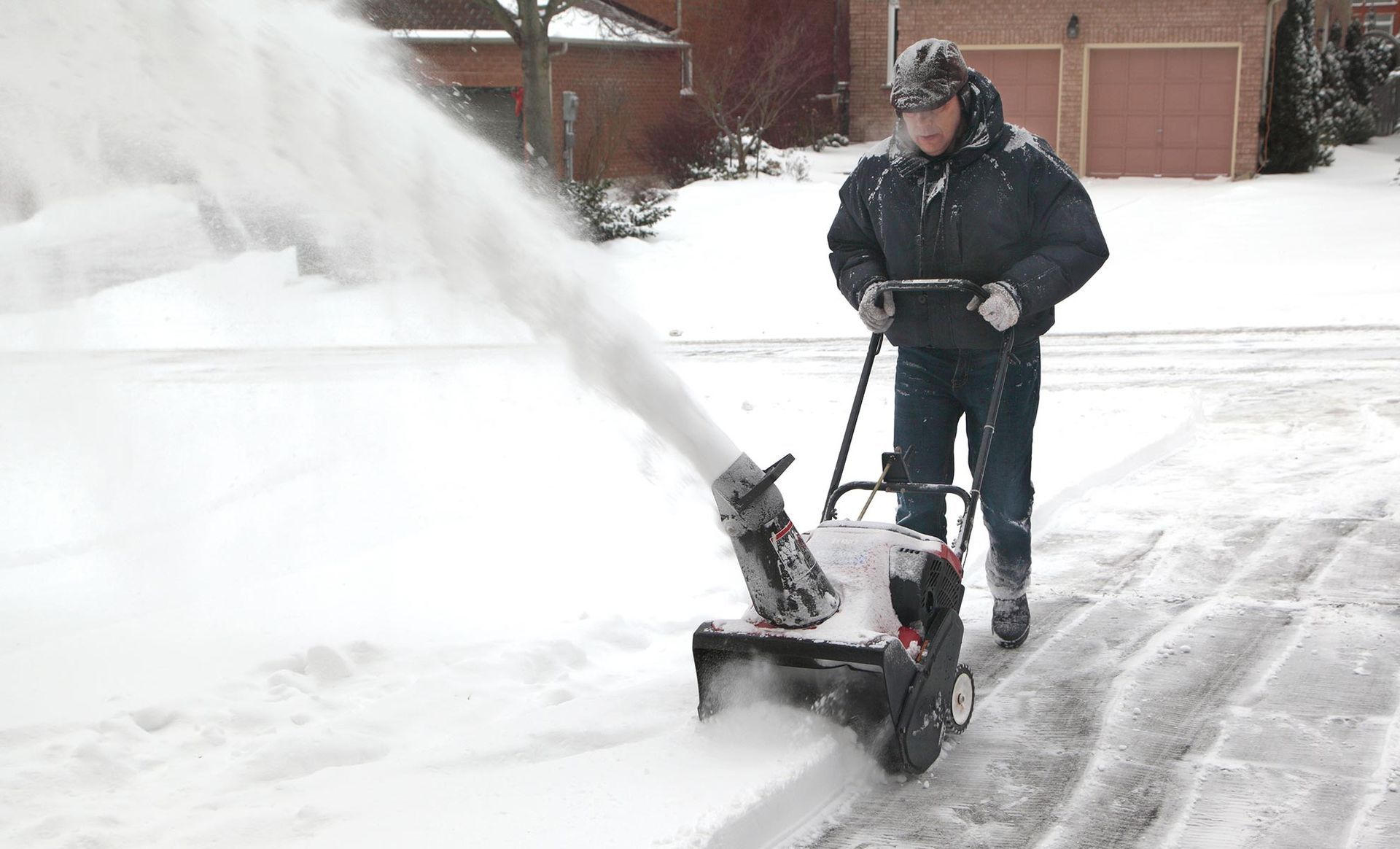 A man is blowing snow from his driveway with a snow blower.