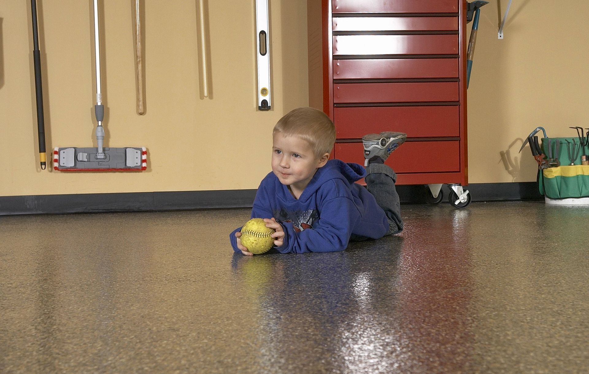 a little boy is laying on the floor in a garage holding a ball