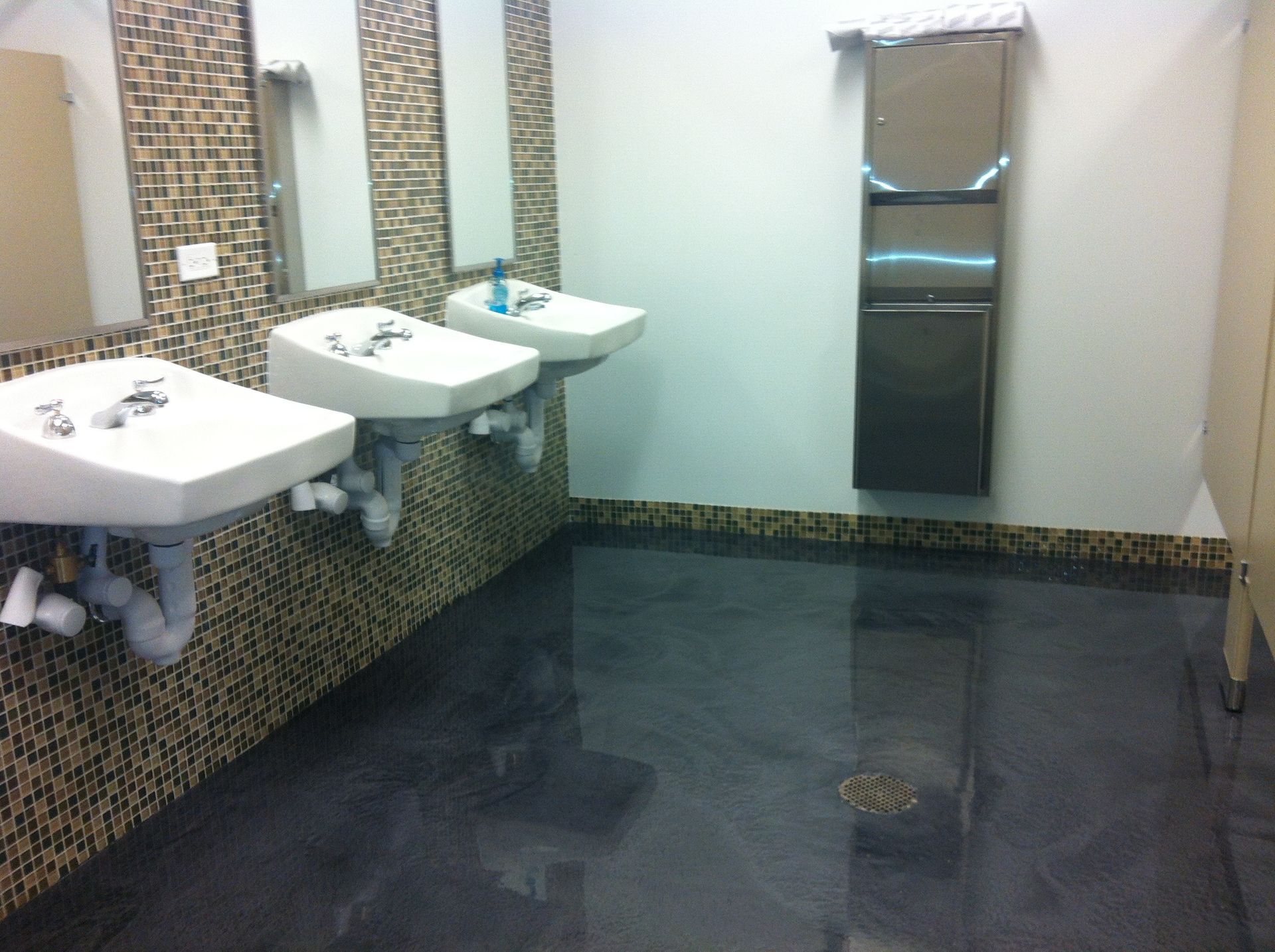 a bathroom with three sinks and a trash can