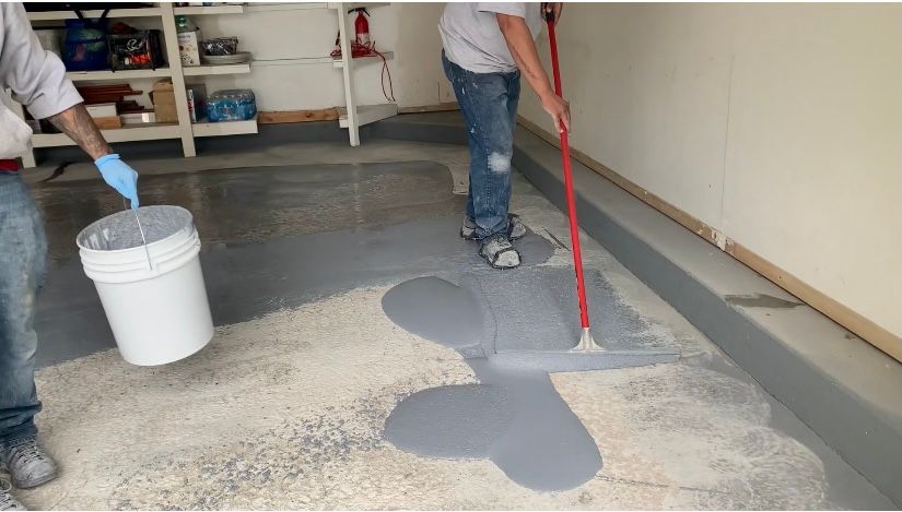 a man is painting the floor of a garage with a mop