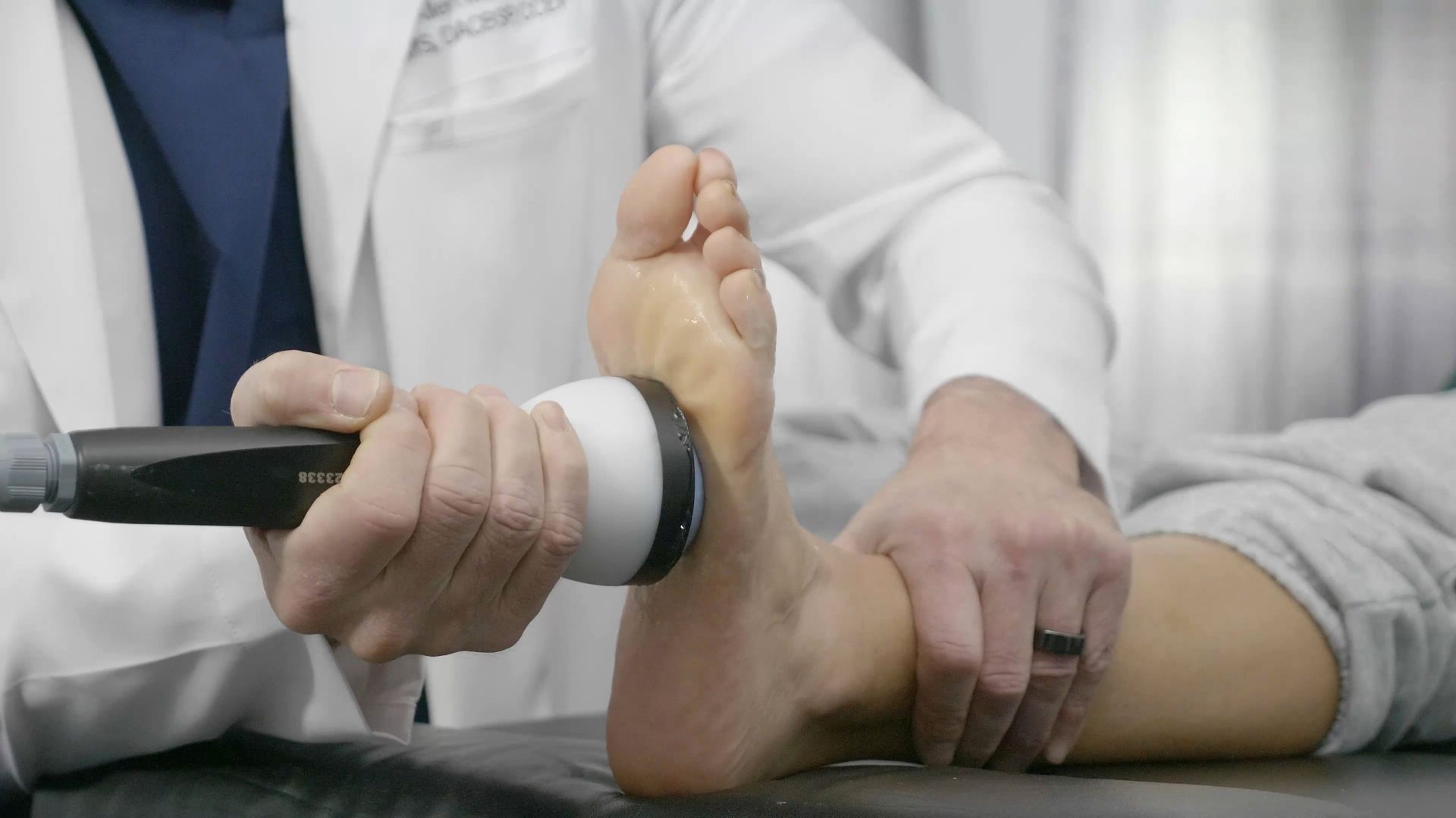 A medical professional uses an ultrasound device on the sole of a patient's foot.