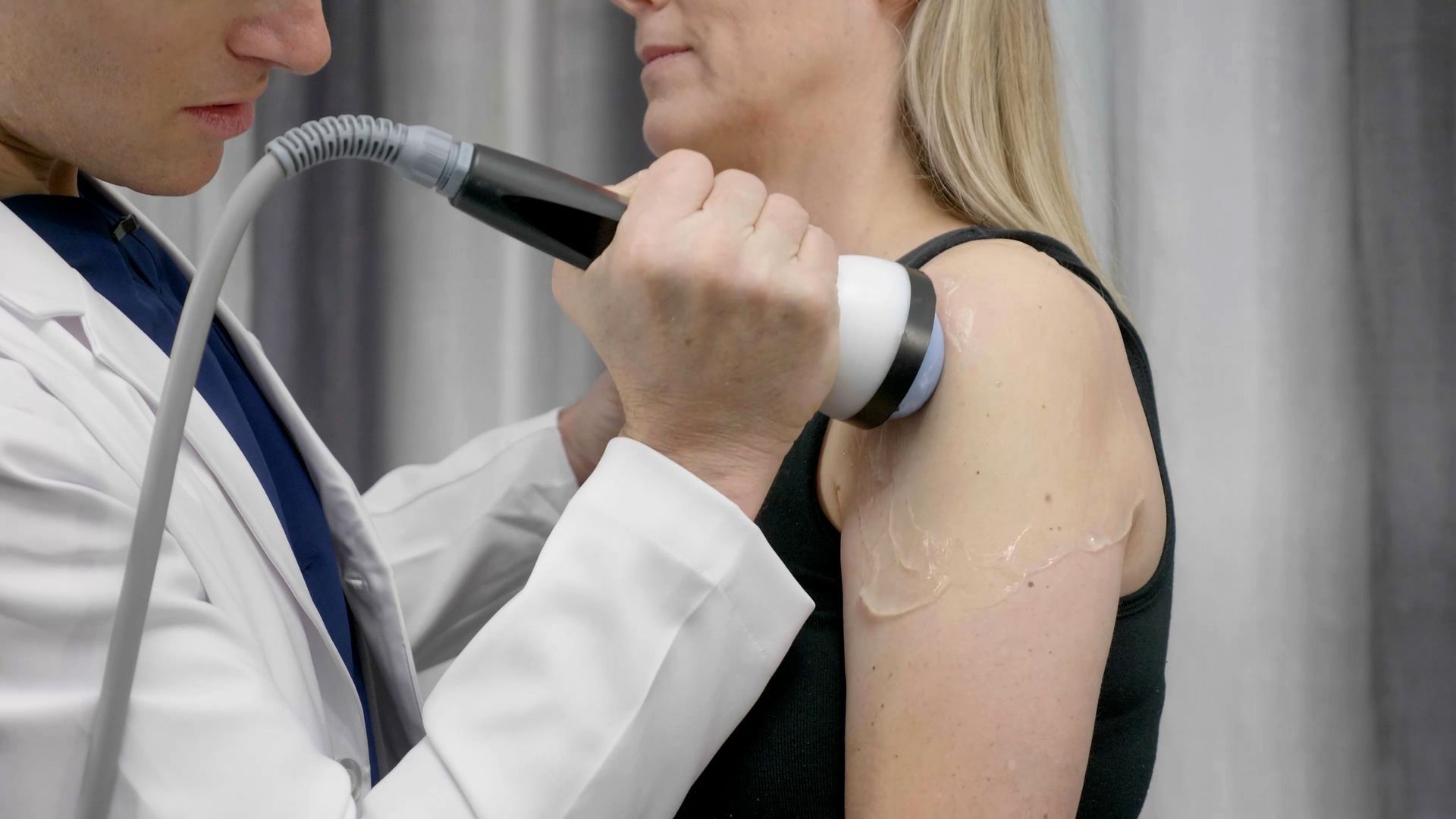 A medical professional using a handheld ultrasound device with conductive gel on a patient's shoulder.