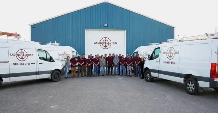 Group of workers posing with vans in front of a blue building with the company logo.