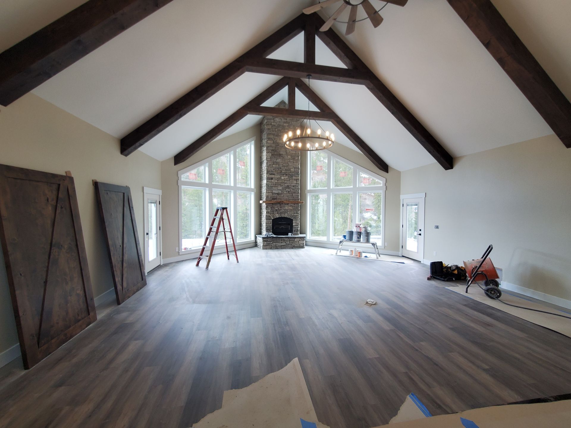 Spacious living room with vaulted ceiling, stone fireplace, large windows, wood beams, and wooden floor.