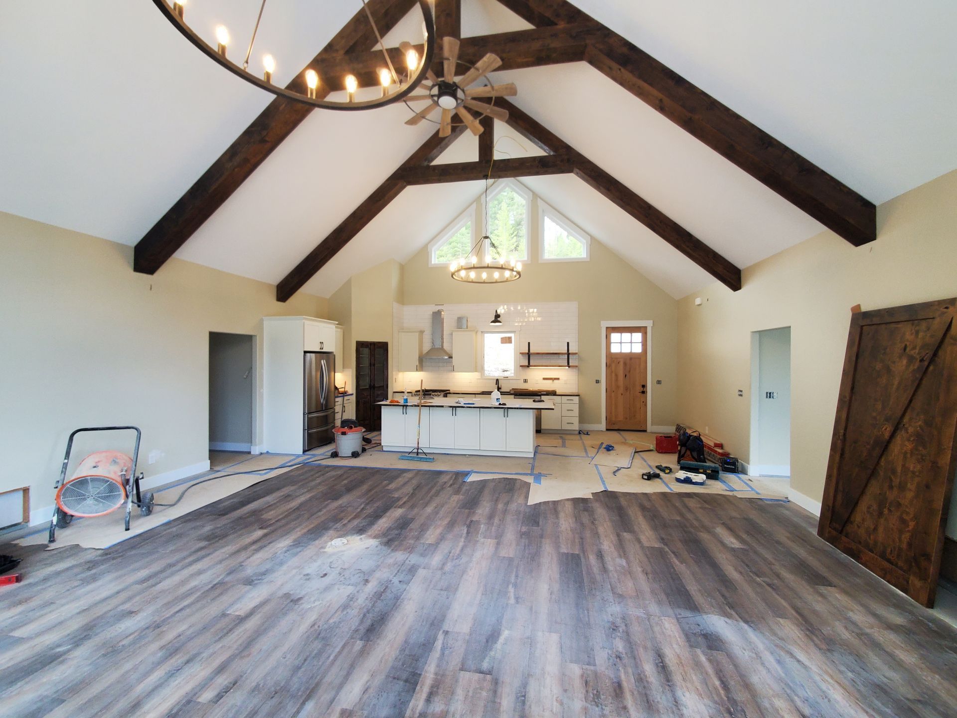 Open-concept kitchen and living area with wood beams, light walls, and dark wood flooring; construction in progress.