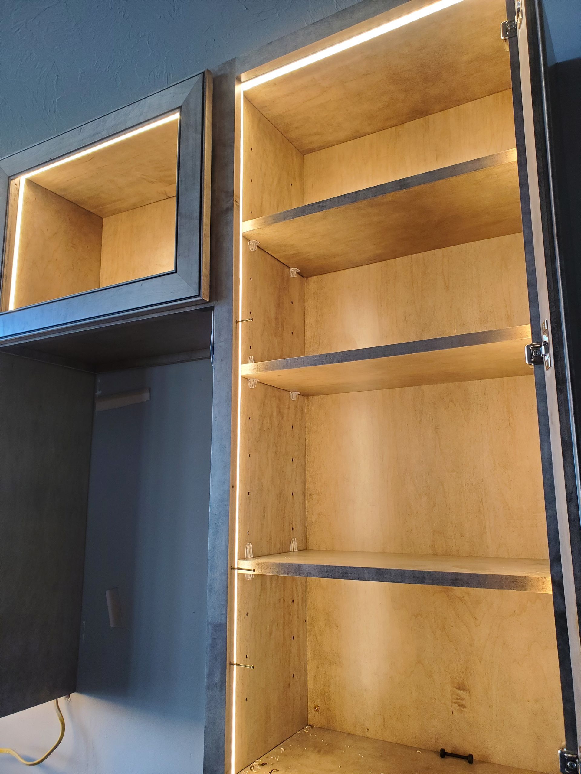 Wooden built-in shelving with warm strip lighting. Cabinet on the left has one shelf, right cabinet has multiple.
