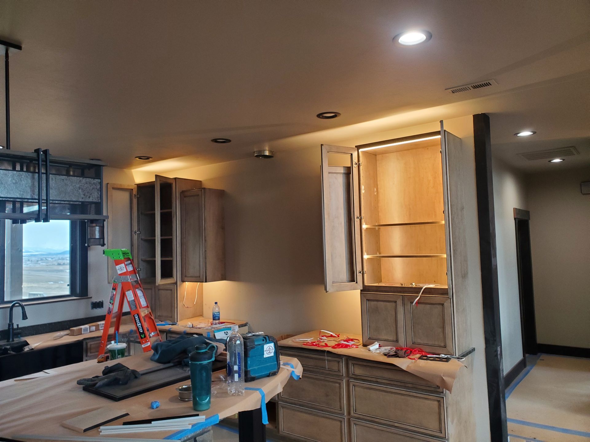 Kitchen under construction with cabinets, lights, and tools.