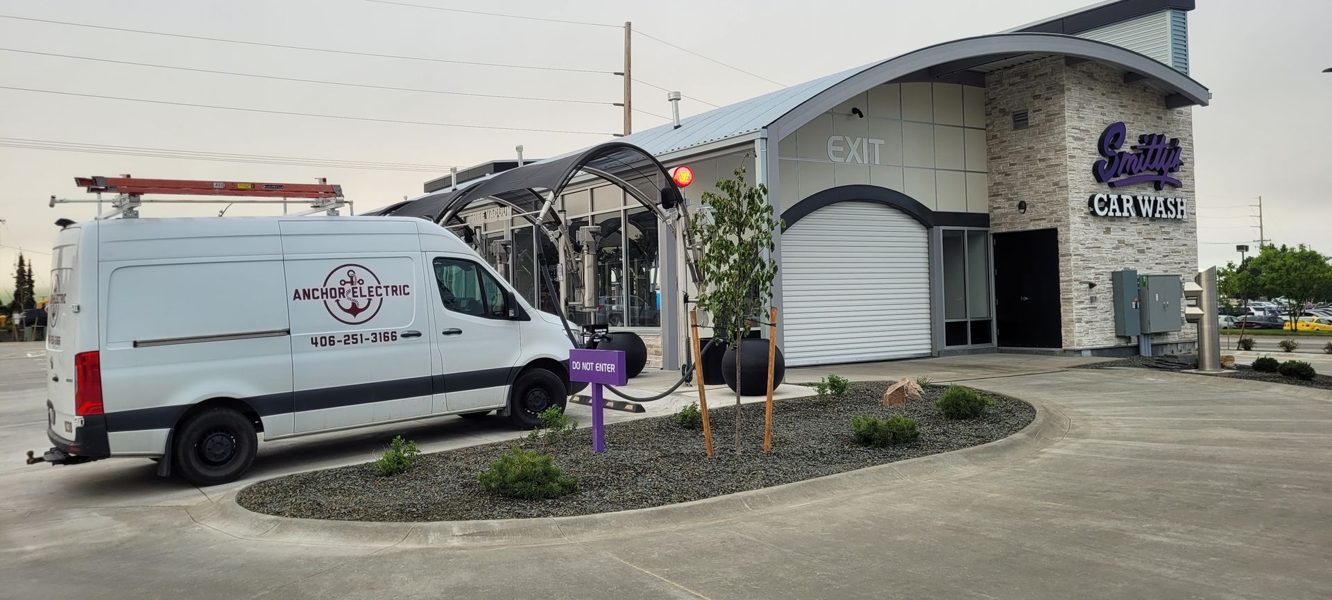 White van parked outside a car wash building. Purple sign in front. Cloudy day.